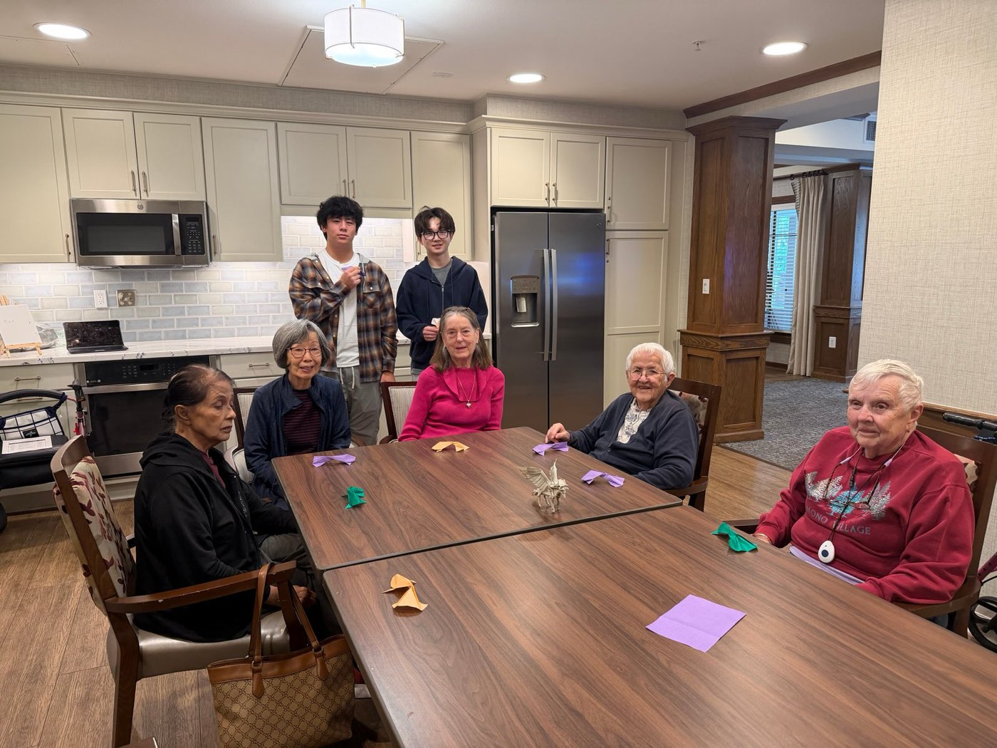 Student volunteers with Ivy Park residents around a table of finished origami
